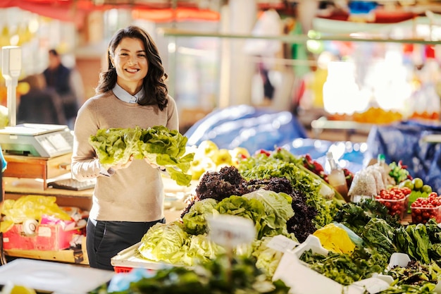 Portrait d'une femme choisissant de la laitue fraîche au marché des agriculteurs et souriant à la caméra