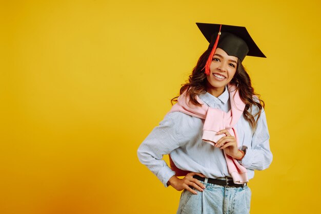 Portrait de femme dans un chapeau de graduation sur sa tête posant sur jaune.