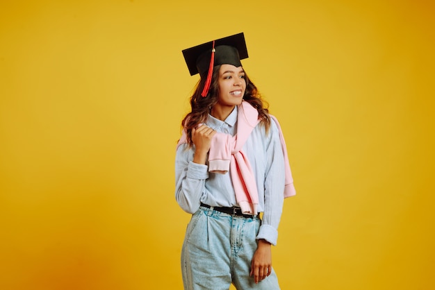 Portrait de femme dans un chapeau de graduation sur sa tête posant sur jaune.