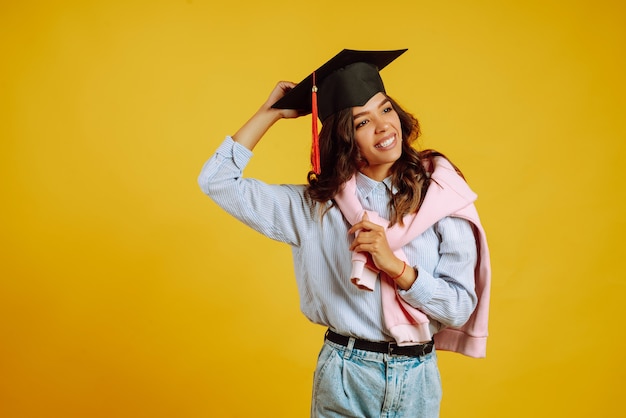 Portrait de femme dans un chapeau de graduation sur sa tête posant sur jaune.