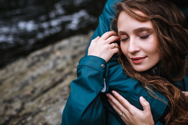 Portrait d'une femme dans un imperméable vert, qui est étreint par son petit ami, contre l'eau