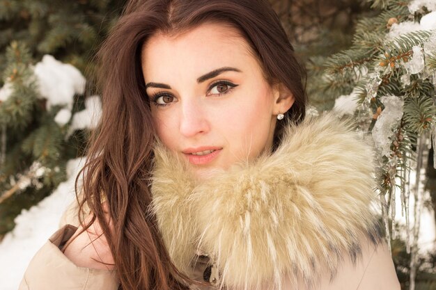 Portrait de femme dans le parc d'hiver près de l'arbre d'hiver