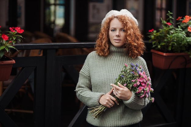 Portrait de femme dans un pull béret tenant un bouquet de fleurs de l'arrière-plan du restaurant