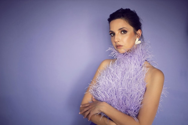 Portrait femme dans une robe violette de soirée avec des plumes se dresse en arrière-plan dans le studio