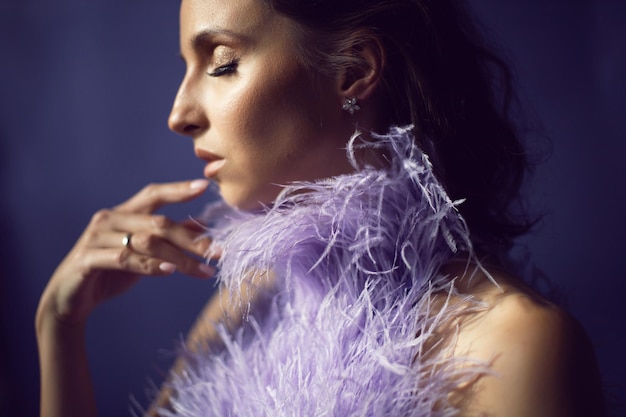 Portrait femme dans une robe violette de soirée avec des plumes se dresse en arrière-plan dans le studio