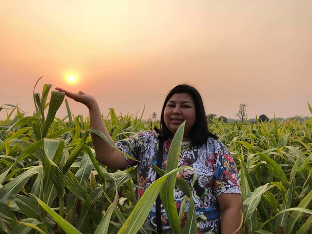 Photo portrait d'une femme debout au milieu des plantes sur le champ au coucher du soleil