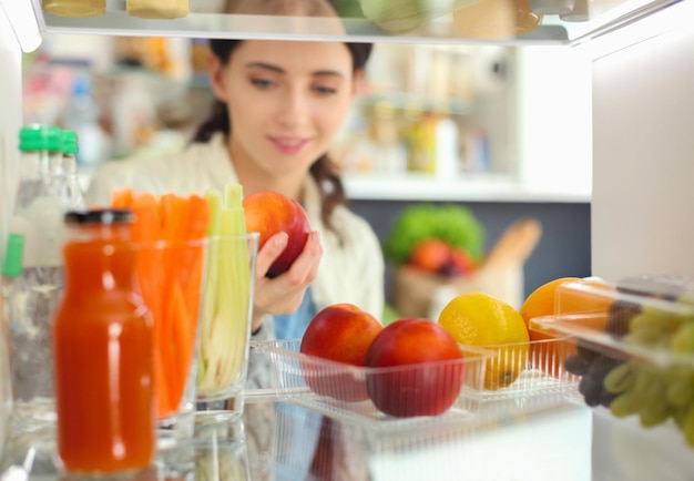 Portrait de femme debout près d'un réfrigérateur ouvert plein de légumes et de fruits sains