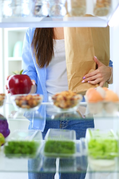Photo portrait de femme debout près d'un réfrigérateur ouvert plein de légumes et de fruits sains