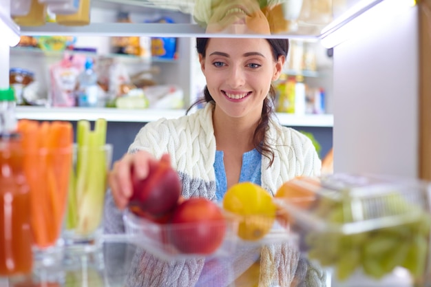 Portrait de femme debout près d'un réfrigérateur ouvert plein de légumes et de fruits sains