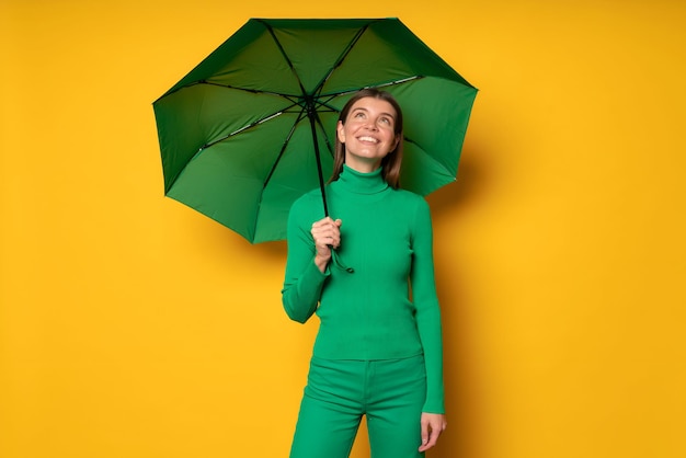 Portrait d'une femme debout sous un parapluie vert sur un fond jaune appréciant un jour de pluie