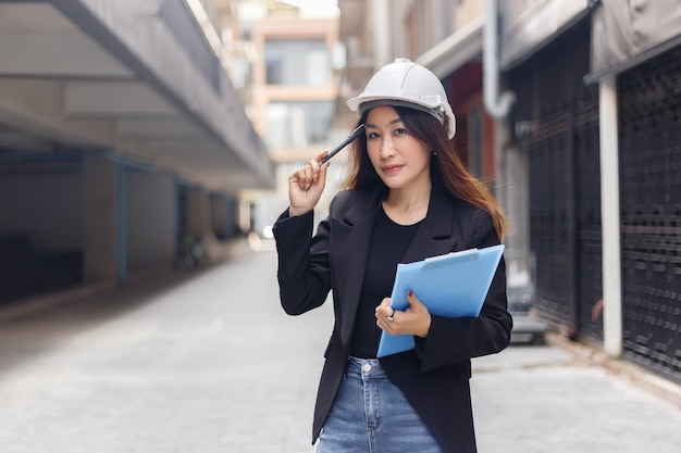 Portrait, une femme développeur d'ingénieurs asiatiques porte un costume noir et un casque de sécurité blanc, un geste réfléchi tenant des documents et un stylo travaillant sur un chantier de construction. copiez l'espace utilisé pour le mot de texte.