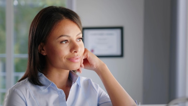 Portrait d'une femme dirigeante afro-américaine habile pensant près de la fenêtre du bureau