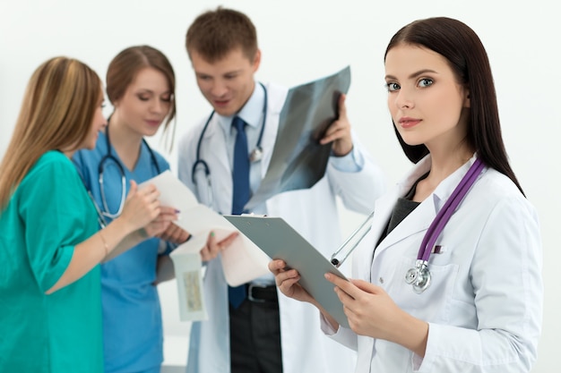 Portrait de femme docteur en médecine brune tenant le dossier de document avec trois de ses collègues regardant le cardiogramme et l'image aux rayons x. Concept de soins de santé et de médecine.