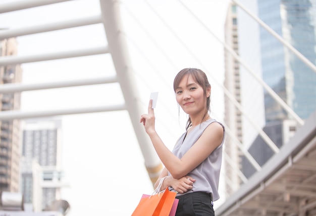 Portrait femme du sourire avec une carte de crédit dans une main en arrière-plan de la ville