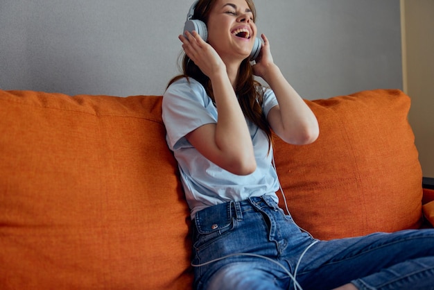 Portrait d'une femme écoutant de la musique avec des écouteurs sur le canapé orange inchangé