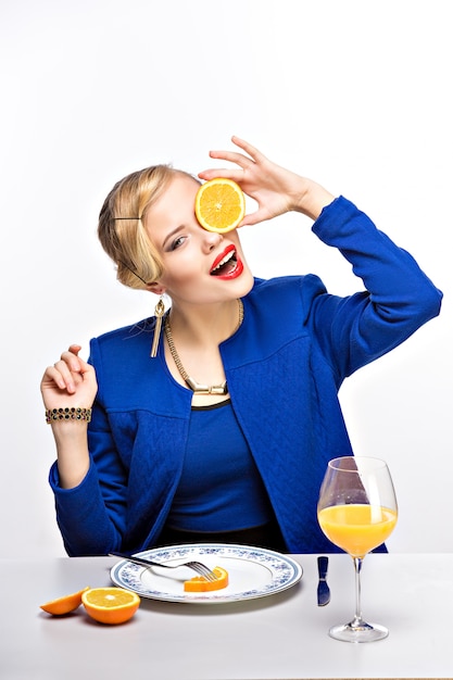 Portrait de femme élégante blonde tenant orange coupée près des yeux