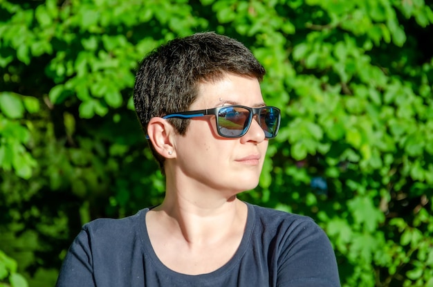 Portrait de femme élégante avec des lunettes de soleil de profil le jour d'été sur fond vert naturel