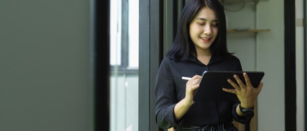 Portrait de femme employée de bureau à l'aide de tablette en se tenant debout dans la salle de bureau