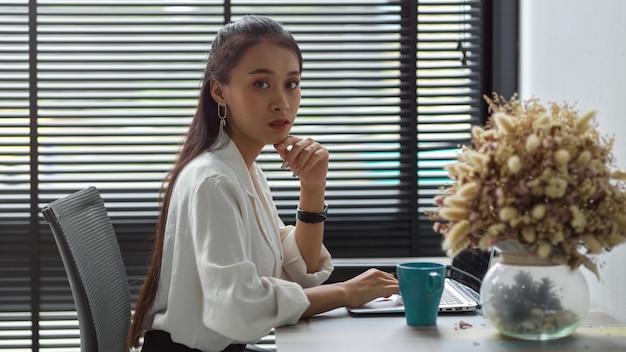 Portrait de femme employée de bureau à la recherche tout en travaillant avec un ordinateur portable sur le bureau