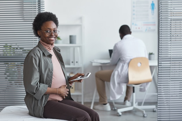 Portrait de femme enceinte africaine souriant à la caméra alors qu'il était assis au cabinet du médecin