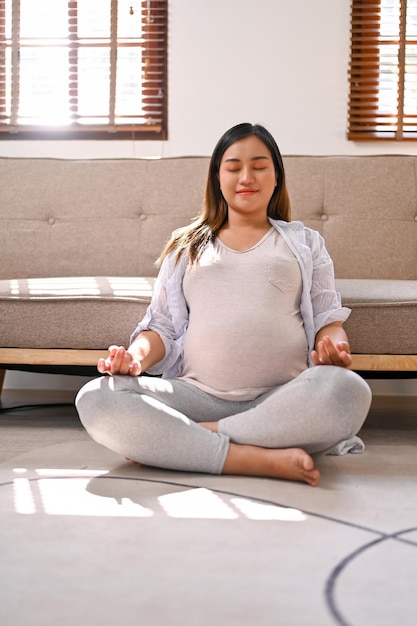 Portrait d'une femme enceinte asiatique heureuse et détendue méditant dans son salon