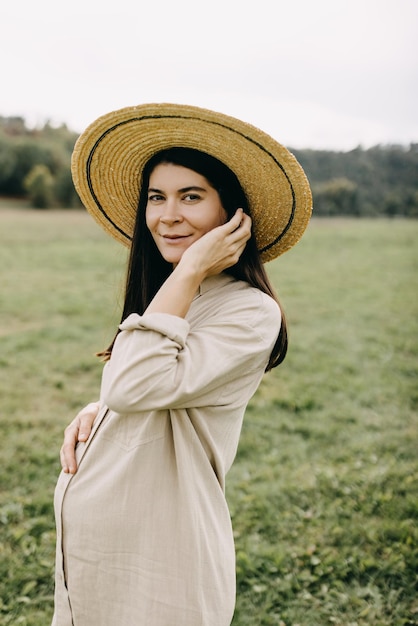 Portrait d'une femme enceinte aux cheveux bruns à l'extérieur dans la nature portant un chapeau de paille