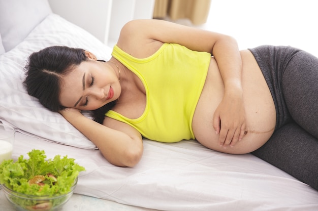 Portrait de femme enceinte en bonne santé allongé sur le lit tout en regardant son ventre