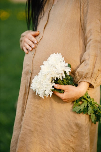 Portrait de femme enceinte dans un parc tenant des fleurs