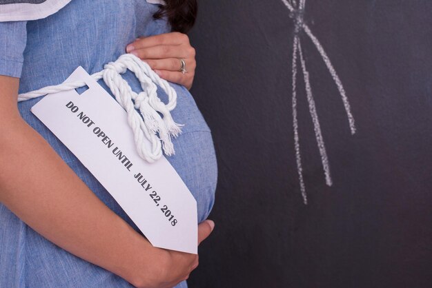 Photo portrait d'une femme enceinte heureuse avec les mains sur le ventre devant un tableau noir