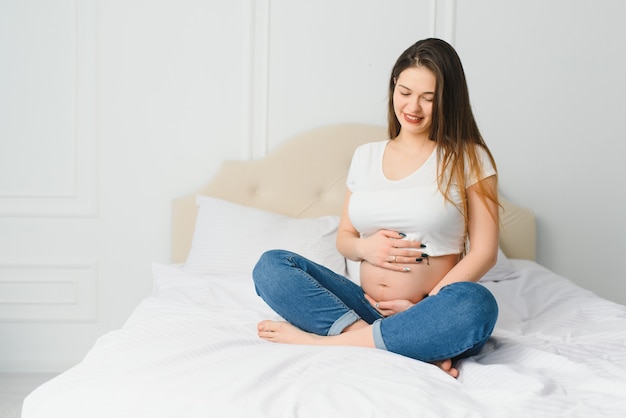 Portrait de femme enceinte joyeuse dans des vêtements décontractés assis sur un divan