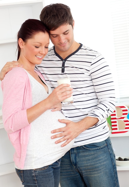 Portrait d&#39;une femme enceinte ravie tenant un verre de lait et de son mari touchant son ventre