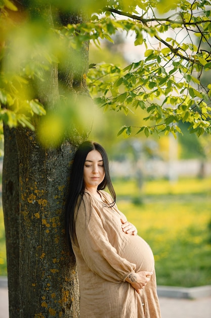 Portrait de femme enceinte en robe beige debout dans un parc