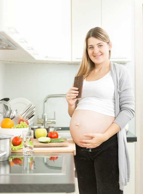 Portrait de femme enceinte souriante posant avec une barre de chocolat dans la cuisine