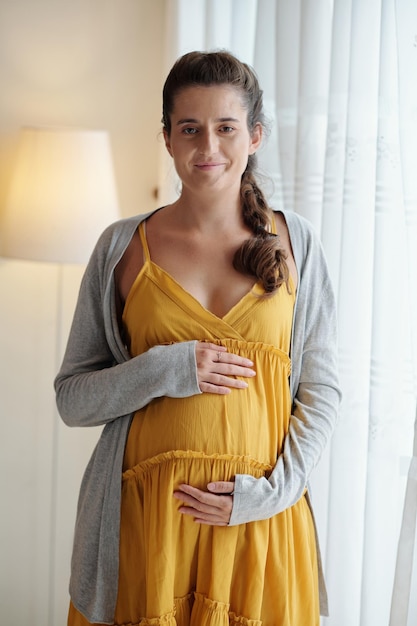 Portrait de femme enceinte souriante touchant le ventre et regardant la caméra