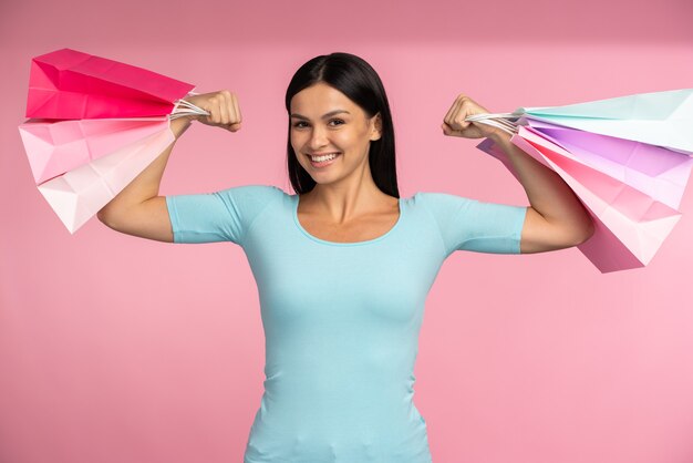 Portrait d'une femme enthousiaste et ravie soulevant des sacs à provisions, se sentant bien avec les colis et célébrant les bas prix. Notion de vendredi noir. Prise de vue en studio, publicité d'un magasin de mode