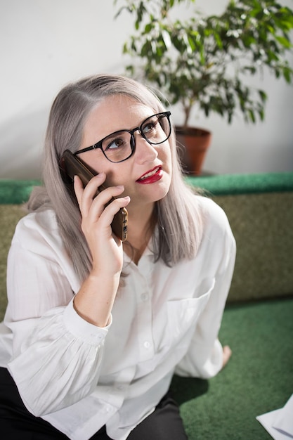 Portrait d'une femme entrepreneure adulte aux cheveux grisâtres dans un poste de direction vêtue d'une blouse blanche et occupée à travailler au bureau