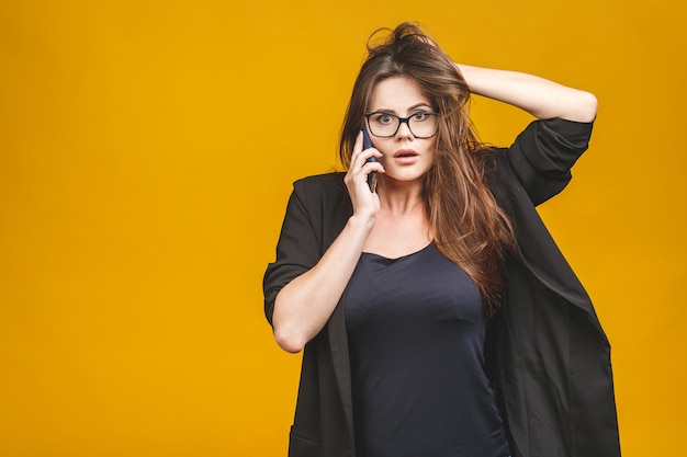 Portrait d'une femme étonnée heureuse en chic décontracté parler au téléphone sur le mur jaune.