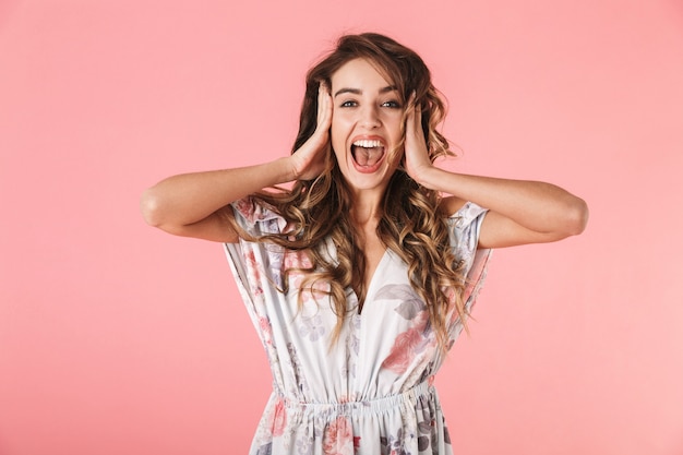 Portrait de femme excitée aux cheveux longs portant une robe debout et hurlant, isolé sur rose