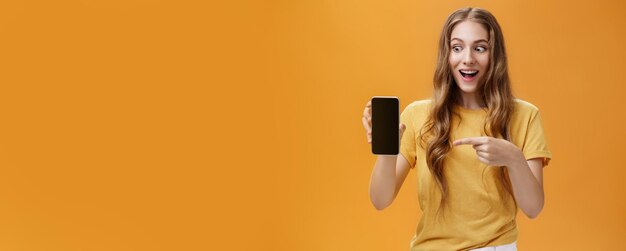 Photo portrait d'une femme excitée se sentant étonnée tenant un nouveau smartphone génial dans la main pointant sur cellphon