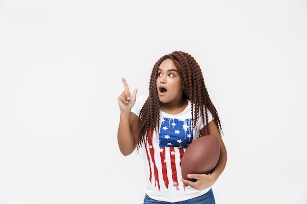 Portrait d'une femme excitée tenant un ballon de rugby pendant le match en se tenant isolé contre un mur blanc