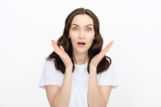 Portrait de femme femme brune en t-shirt blanc avec la bouche ouverte de surprise sur fond blanc nouvelles choc surprise