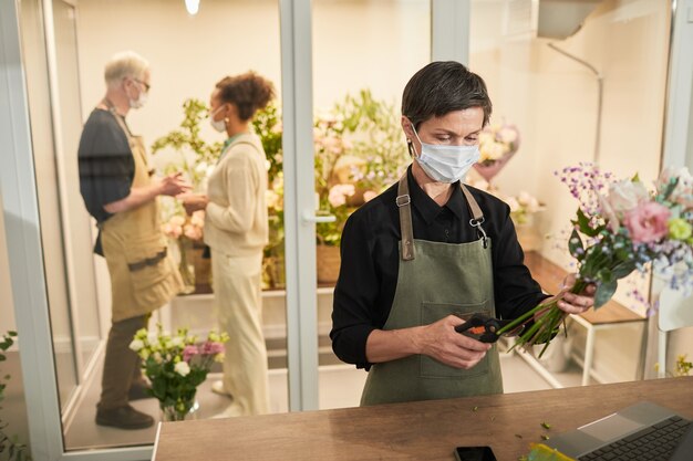 Portrait de femme fleuriste portant un masque tout en organisant des bouquets dans l'espace de copie du magasin de fleurs