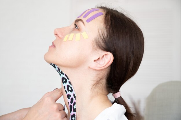 Portrait d'une femme sur fond blanc avec un kinesiotape du visage et du cou. Concept de bande esthétique.