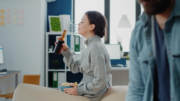 Portrait d'une femme avec des frites et une bouteille de bière après le travail, regardant des collègues jouer au baby-foot. Personne appréciant des boissons et des collations pour célébrer avec une activité amusante après les heures