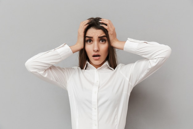 Portrait de femme frustrée en robe formelle saisissant sa tête en panique ou problème, mur blanc gris isolé