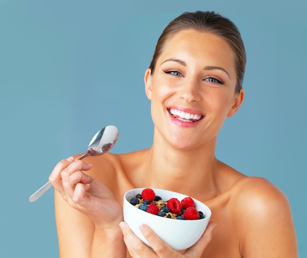 Portrait de femme et heureuse avec des céréales en studio pour une digestion saine des repas bénéficie de l'alimentation et de la nutrition Le petit déjeuner souriant et le modèle de fitness féminin isolé sur fond bleu et mangeant de la nourriture dans un bol