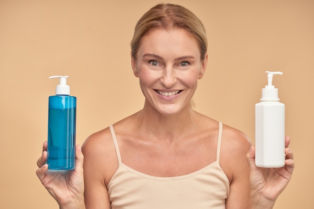 Portrait d'une femme heureuse choisissant entre deux produits de soins corporels en se tenant isolée sur