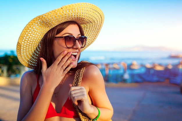Portrait d'une femme heureuse et excitée au chapeau marchant sur la plage au coucher du soleil Vacances d'été
