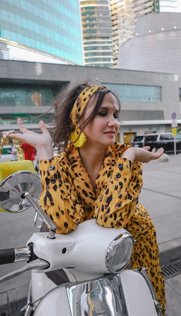 Un portrait d'une femme heureuse habillée à la mode posant pour une séance photo sur un cyclomoteur