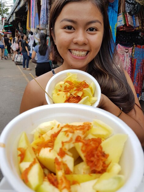 Photo portrait d'une femme heureuse montrant de la nourriture dans un récipient au marché du week-end de chatuchak